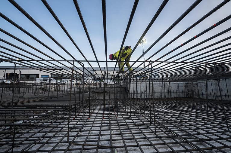 Reinforced concrete construction site with steel rebar framework and worker welding, focusing on concrete building foundations and industrial infrastructure.