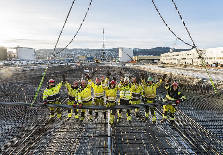 High-angle view of construction workers in safety gear standing on reinforced concrete foundation at a building site, showcasing construction and concrete pouring services.