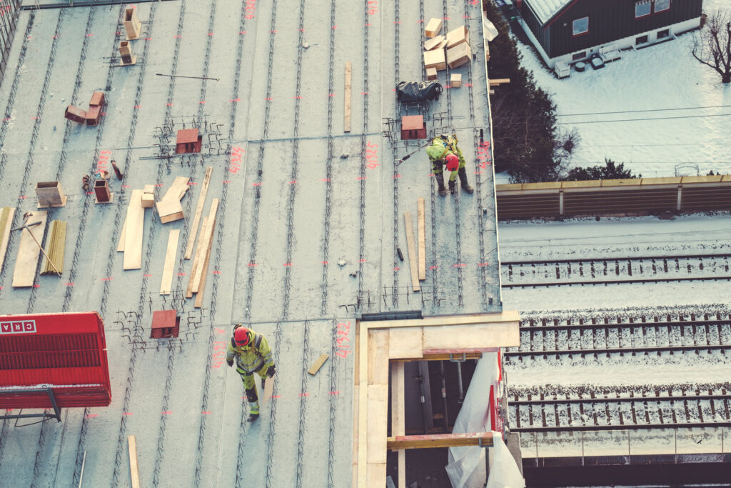 Reinforced concrete construction site with workers, showing building framework and snowy surroundings.