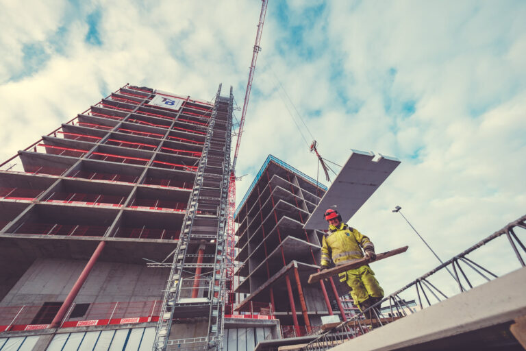 Reinforced concrete building under construction with a worker in safety gear on site, showcasing Trio Betong's expertise in concrete and construction solutions for high-rise projects.