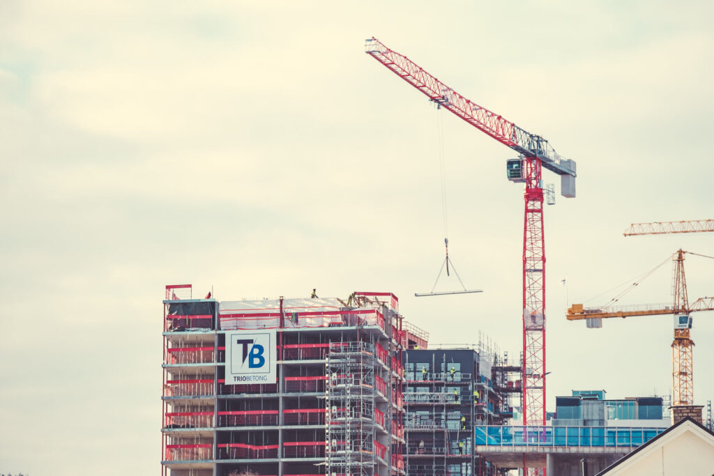 Overhead view of a multi-story concrete building under construction with cranes and construction workers on site.