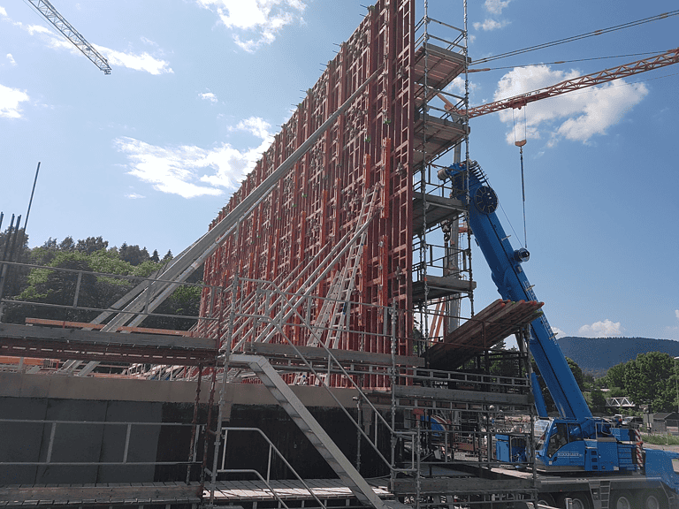 Precast concrete formwork and construction site with scaffolding and tower crane at a building project.